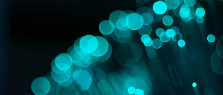 Imagen de fondo oscuro con un efecto de luces bokeh en tonos azul turquesa brillante, que simulan destellos de fibra óptica o reflejos suspendidos en el aire.